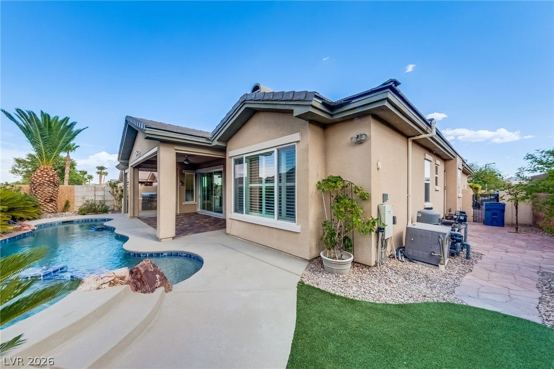 An inviting backyard retreat features a curved in-ground pool alongside a covered concrete patio.