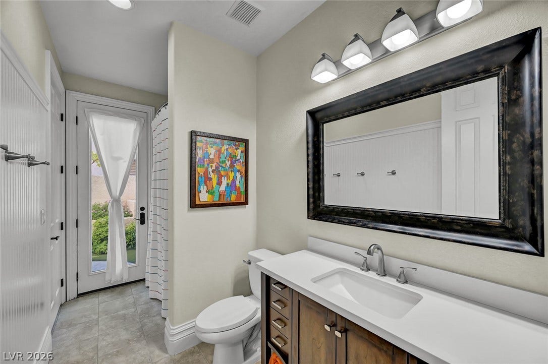 1116 Golden Age Court, Las Vegas, NV 89144 A classic vanity with stone counters and a wood cabinet anchors this light-filled bathroom.