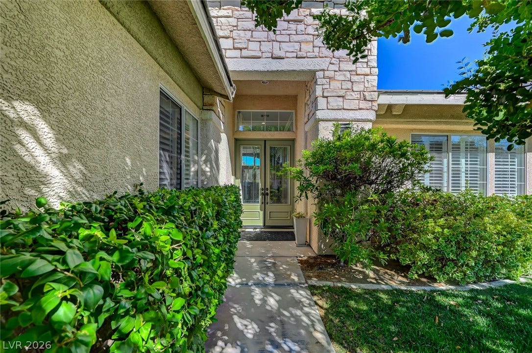 1116 Golden Age Court, Las Vegas, NV 89144 A stone-accented entryway leads to double doors framed by manicured hedges and mature trees.