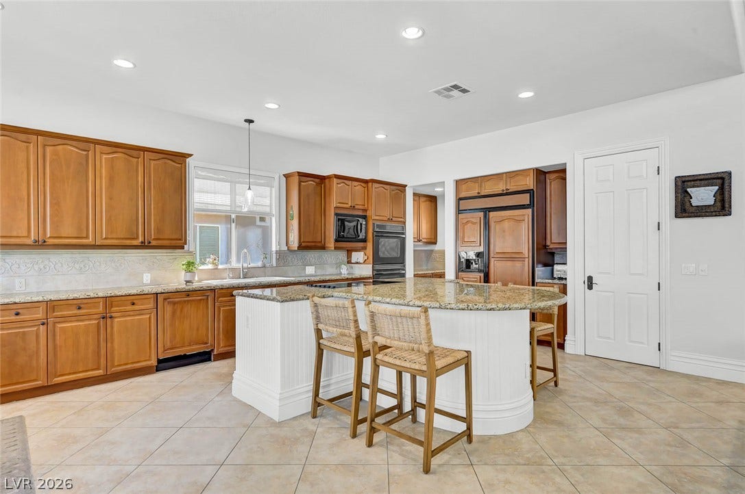 1116 Golden Age Court, Las Vegas, NV 89144 Gleaming stone countertops and a spacious curved island anchor this well-appointed culinary space.