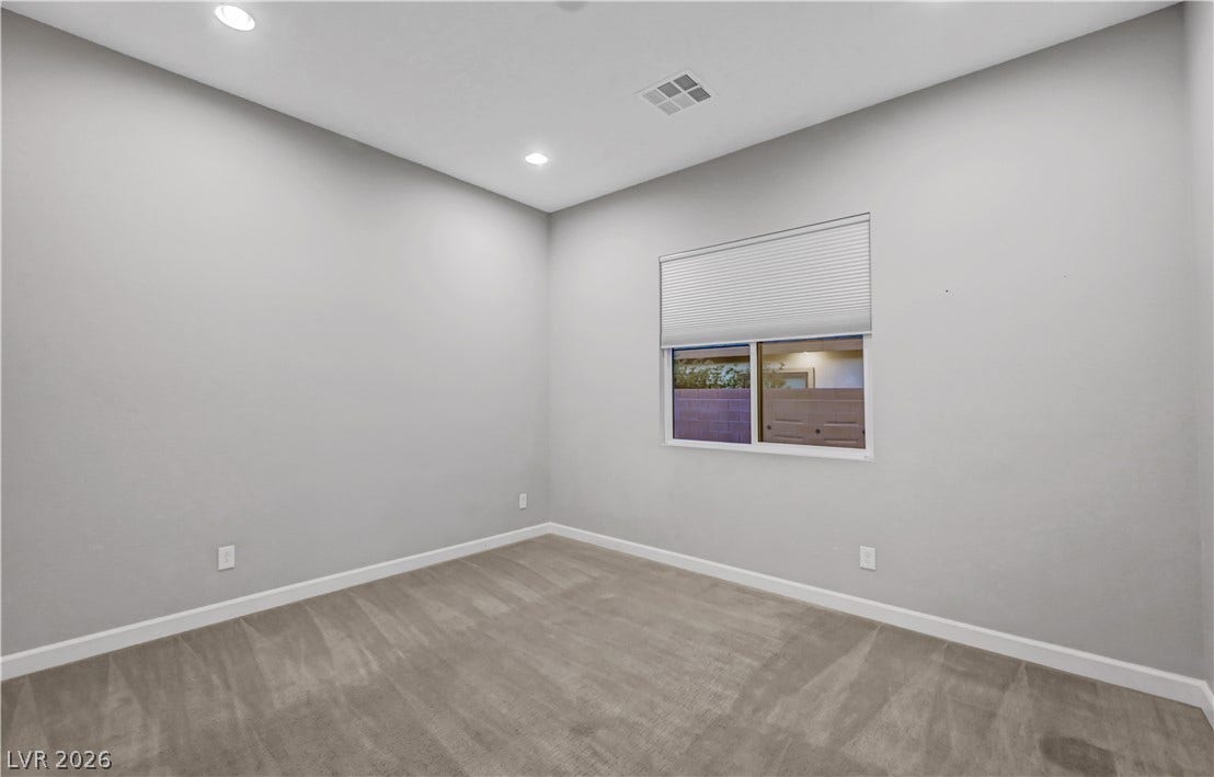 Recessed lighting illuminates this clean bedroom space with soft neutral carpeting and high ceilings.