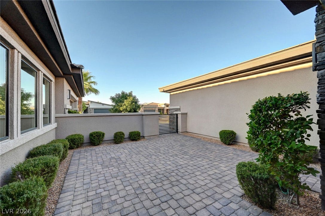 Neat pavers and low hedges line this gated entrance courtyard under clear blue skies.