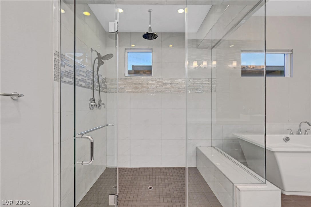 A glass-enclosed shower with custom tile surrounds stands next to a freestanding soaking tub.