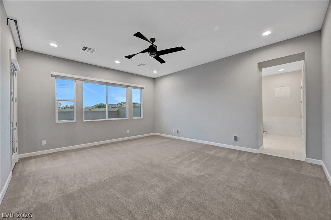 A spacious carpeted bedroom features recessed lighting and an adjoining bathroom doorway.