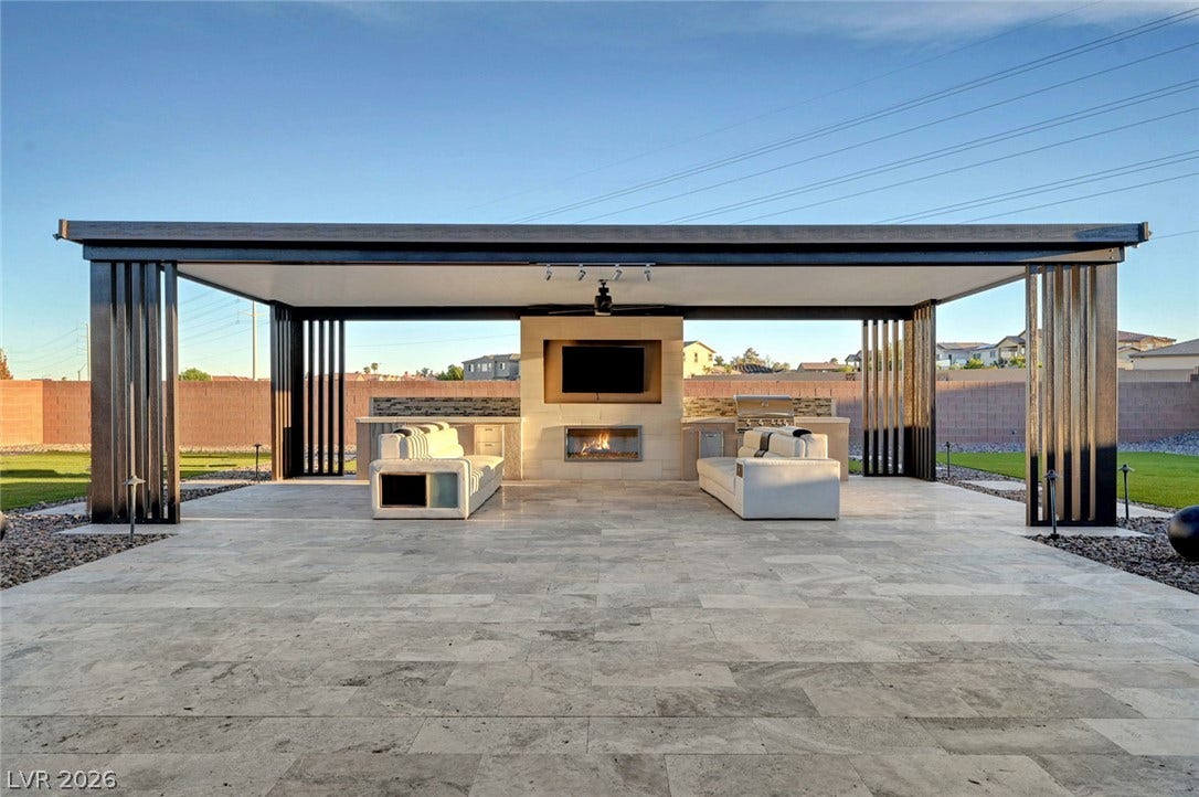 An open-air pavilion anchors this tiled patio complete with a stone fireplace and outdoor kitchen.