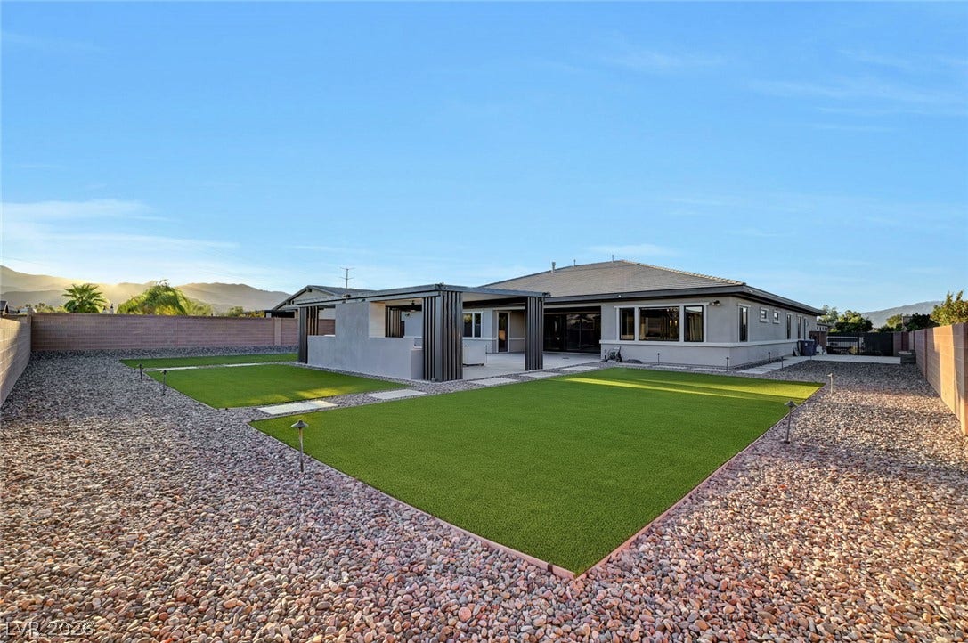 A spacious backyard with desert landscaping and manicured lawn highlights this modern single-story residence.