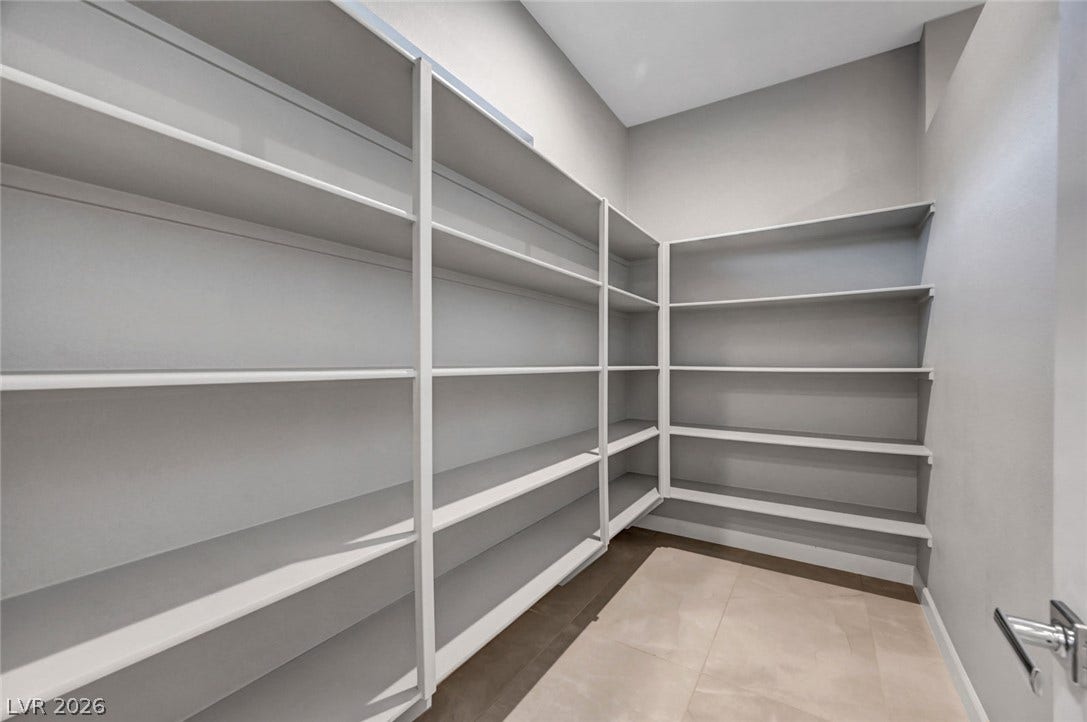 Extensive built-in shelving lines this walk-in storage area featuring large-format tile flooring.