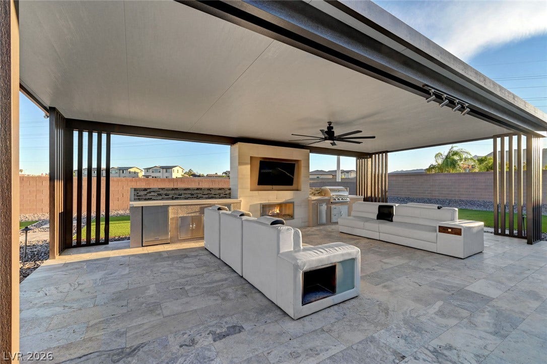 An covered outdoor patio includes stone tile flooring and a built-in stone fireplace.