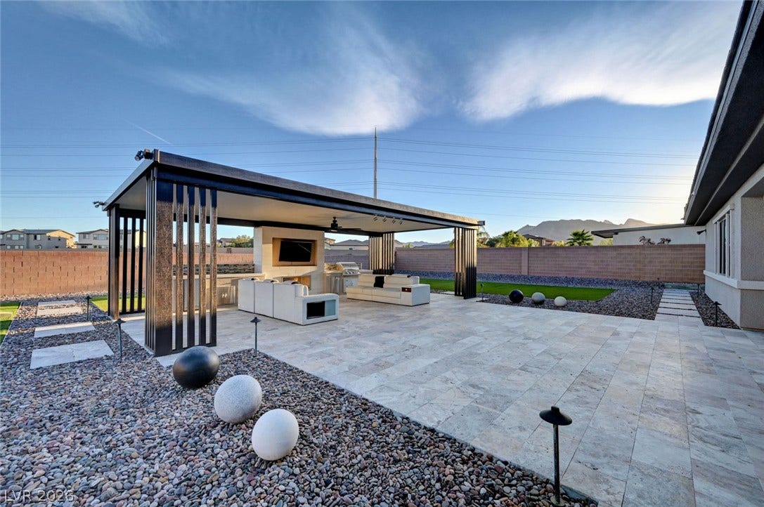 An expansive paved patio features a covered modern pavilion beneath clear desert skies.