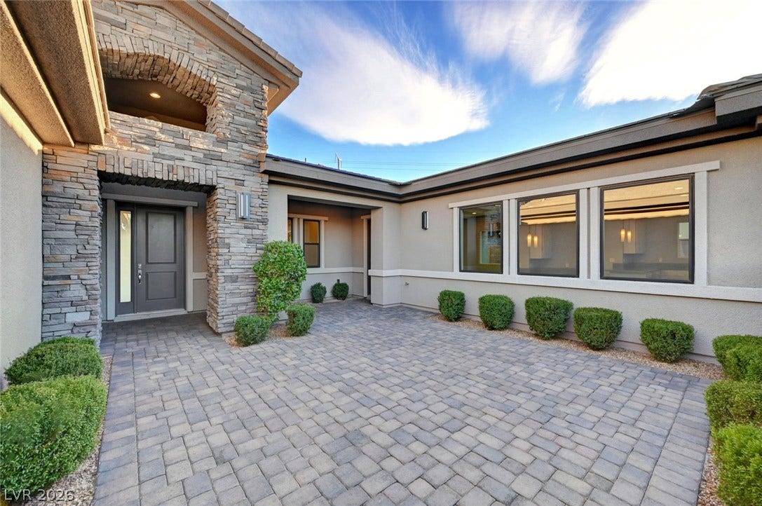 An inviting stone entryway accents the paved courtyard of this modern single-story residence.