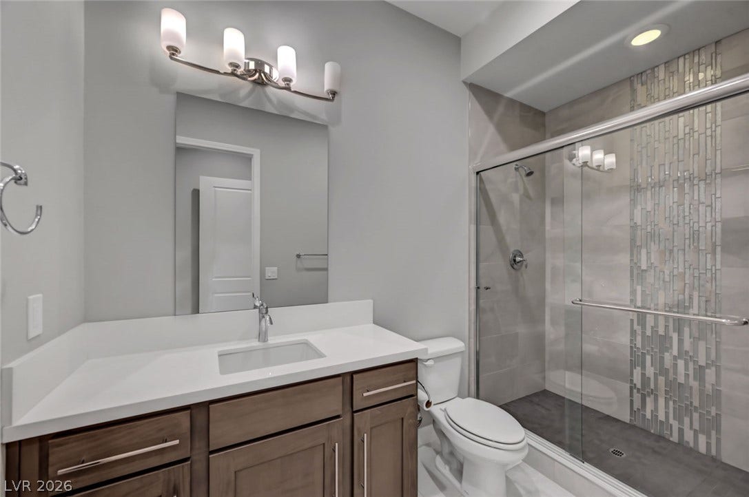 A modern vanity with stone counters complements a sleek tiled walk-in shower with sliding glass doors.