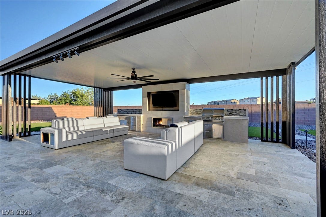 An expansive covered patio features tiled flooring, a built-in kitchen, and a modern fireplace.