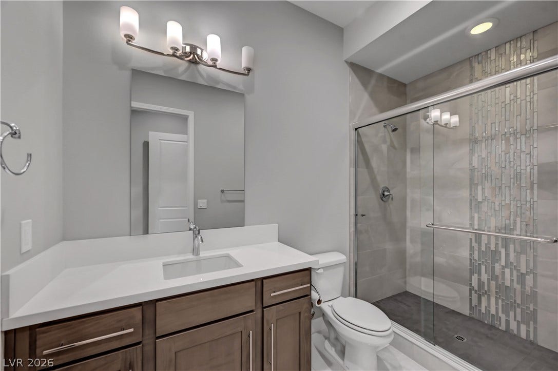 An elegant bathroom features a glass-enclosed shower with vertical accent tiling and a modern vanity.