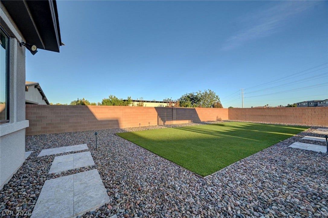 A spacious backyard features manicured turf surrounded by low-maintenance desert rock landscaping.
