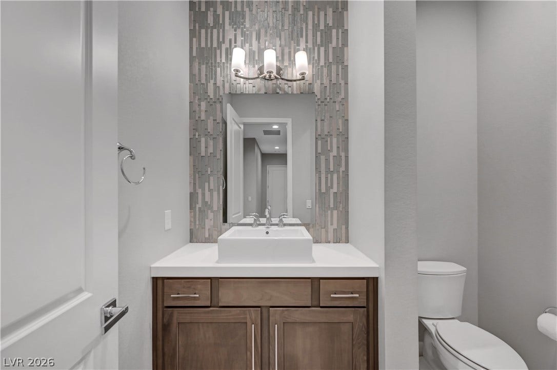 A vessel sink rests on a wood vanity set against a patterned tile accent wall.