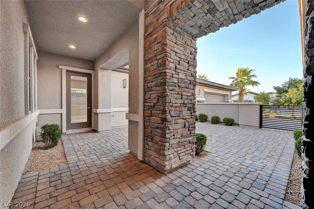 An inviting stone archway frames a paved courtyard leading to the private glass entryway.