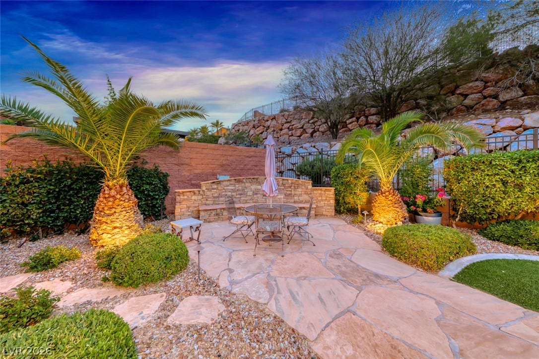 41 Moltrasio Lane, Henderson, NV 89011 Lush palm trees flank a flagstone patio set against a natural stone retaining wall.