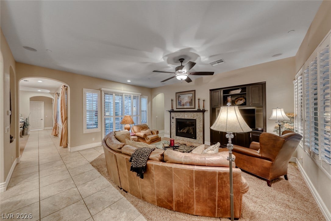 41 Moltrasio Lane, Henderson, NV 89011 A warm fireplace anchors this spacious living area alongside tile flooring and classic plantation shutters.