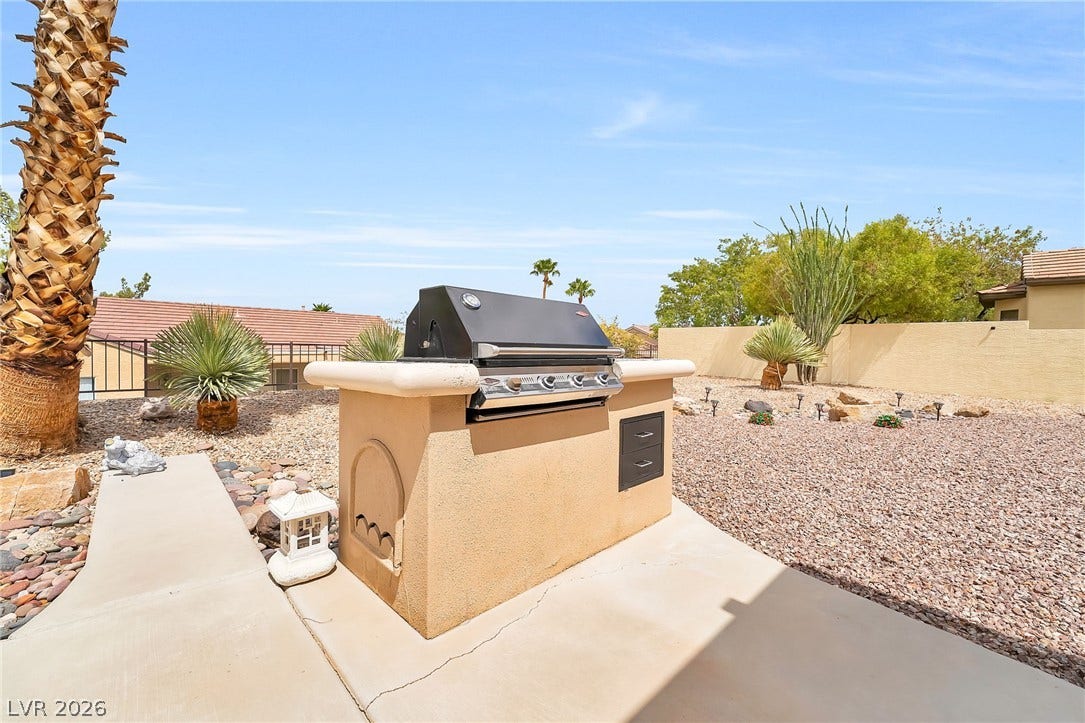 An outdoor grilling station sits on a concrete patio overlooking a desert landscape yard.