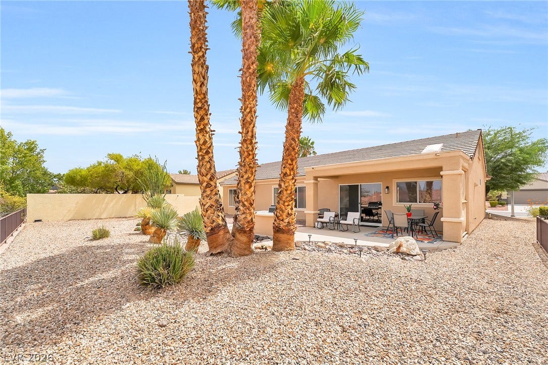 Lush palm trees and desert landscaping frame the covered patio of this stucco home.