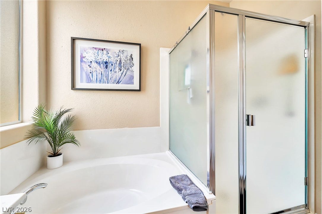 An inviting corner soaking tub sits adjacent to a frosted glass walk-in shower enclosure.
