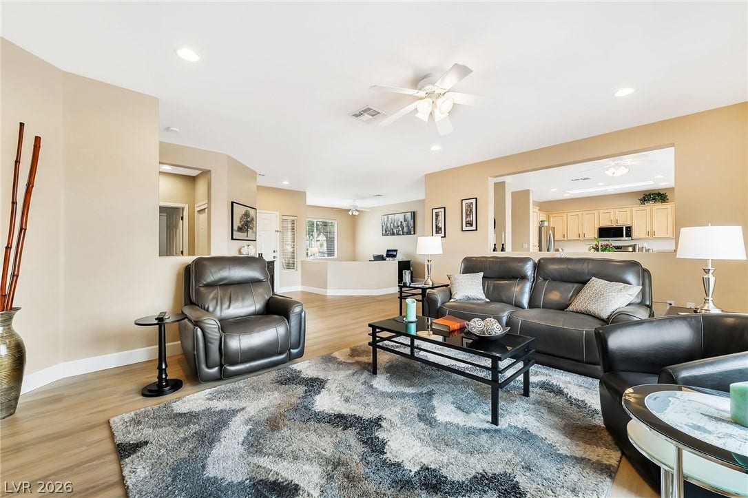 An open-concept living area flows seamlessly into the kitchen under recessed lighting and wood-style flooring.