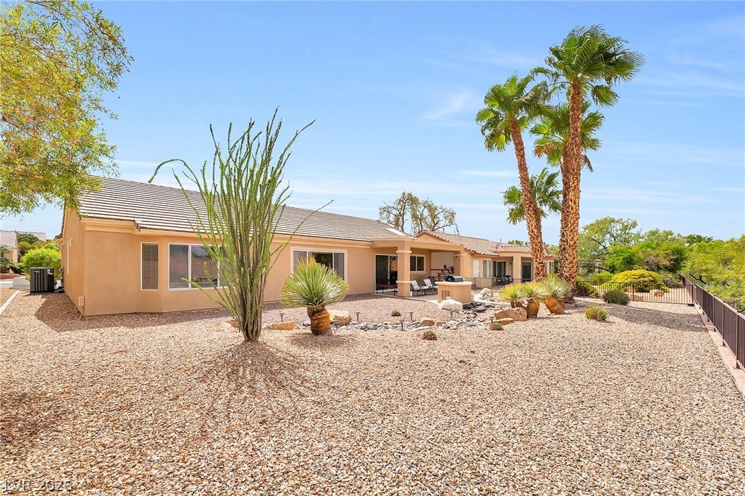 Desert landscaping and mature palms frame the back of this single-story stucco residence.