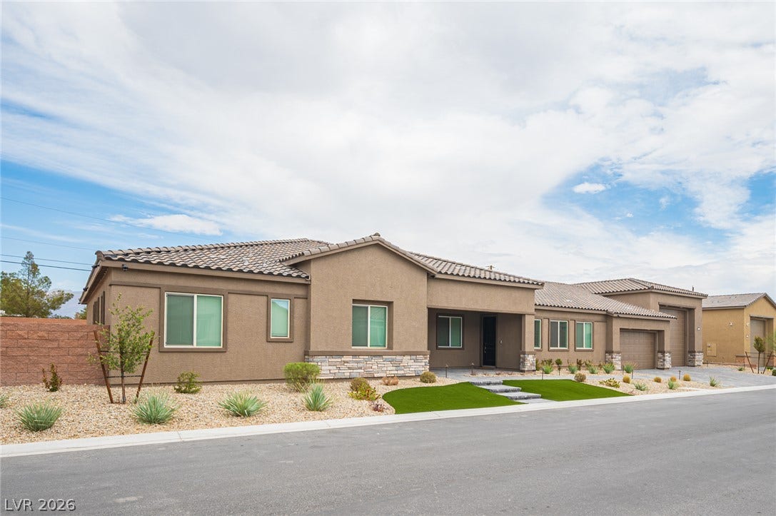 3904 Aiden Creek Avenue, North Las Vegas, NV 89031 A modern facade features textured stucco, stone accents, and desert landscaping under wide blue skies.