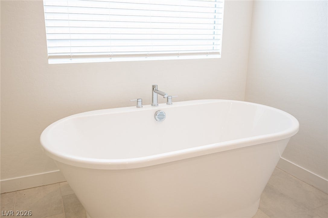 3904 Aiden Creek Avenue, North Las Vegas, NV 89031 A deep soaking tub sits beneath a large window in this relaxing bathroom space.