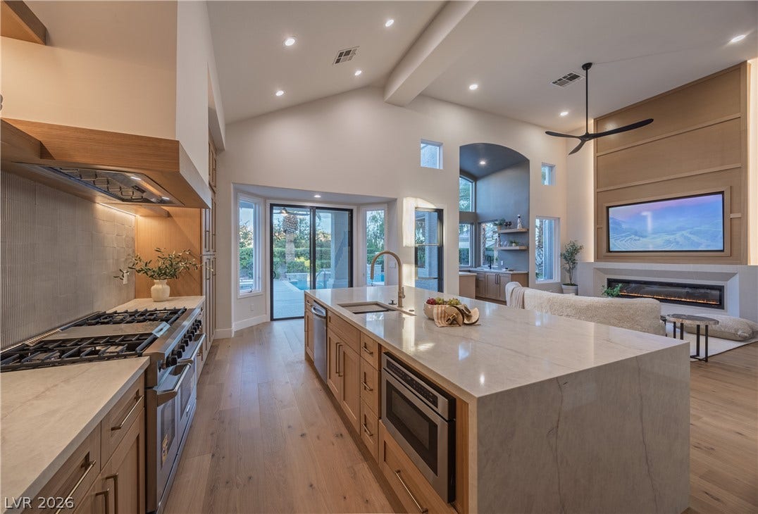 8800 Lusso Court, Las Vegas, NV 89134 Kitchen featuring stainless steel appliances, light stone counters, light wood-style flooring, open floor plan, and a glass covered fireplace