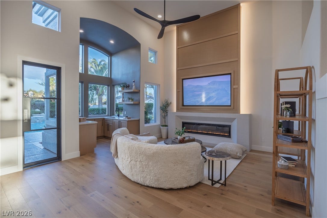8800 Lusso Court, Las Vegas, NV 89134 Living area with a high ceiling, a glass covered fireplace, light wood finished floors, a ceiling fan, and healthy amount of natural light