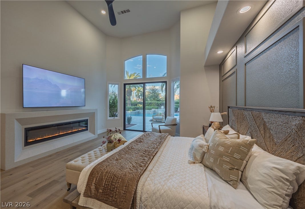 8800 Lusso Court, Las Vegas, NV 89134 Bedroom with access to exterior, light wood-type flooring, a glass covered fireplace, recessed lighting, and a high ceiling