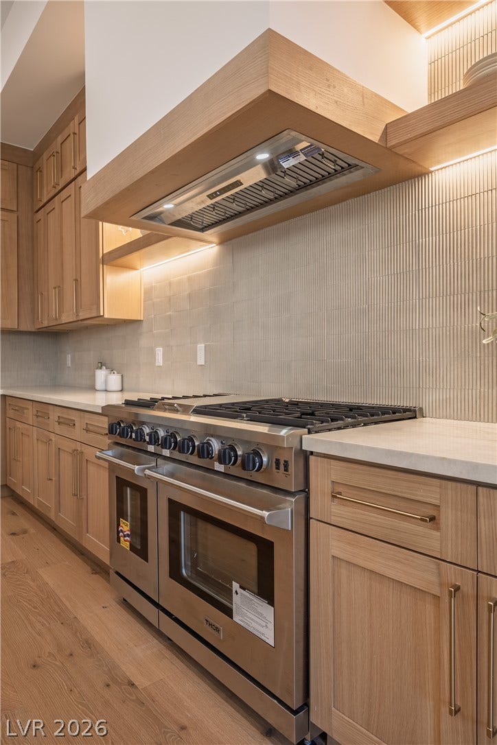 8800 Lusso Court, Las Vegas, NV 89134 Kitchen with double oven range, light wood-style floors, backsplash, light stone countertops, and light wood finish cabinetry