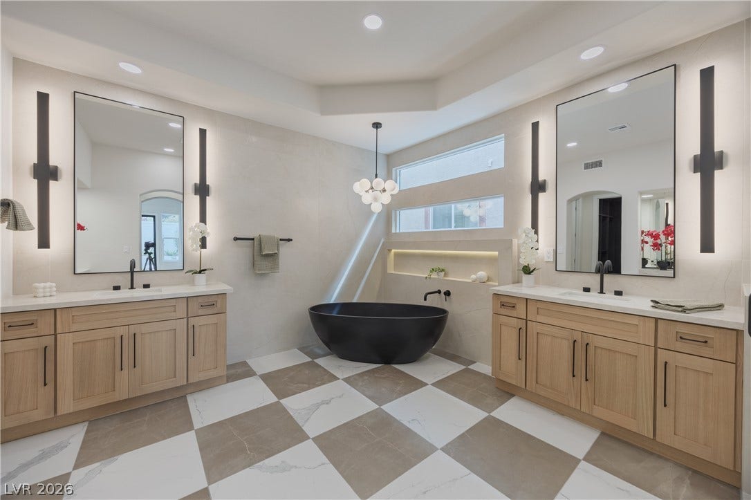 Full bathroom featuring two vanities, a freestanding bath, suspended lighting, and plenty of natural light
