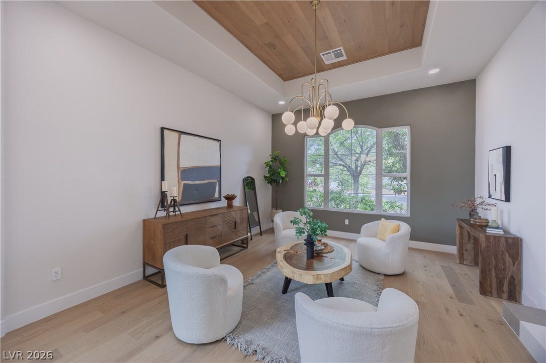 Living area with a wood tray ceiling, hanging lights, and light wood-style floors