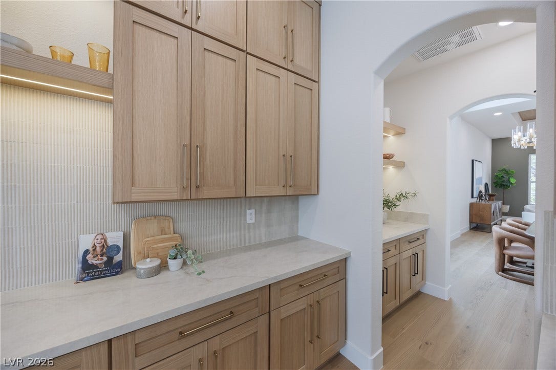 Kitchen featuring light stone counters, light wood-style floors, open shelves, arched walkways, and light wood finish cabinetry