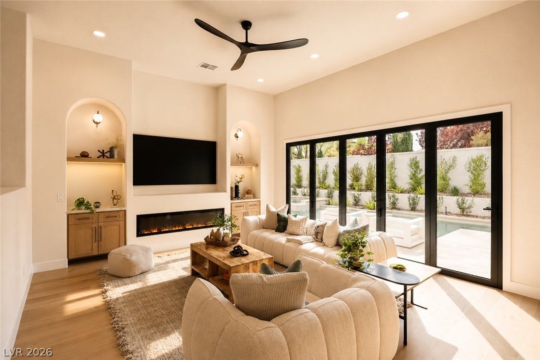 A living area with light wood flooring and a modern fireplace offers expansive views of the outdoor pool through large folding glass doors.