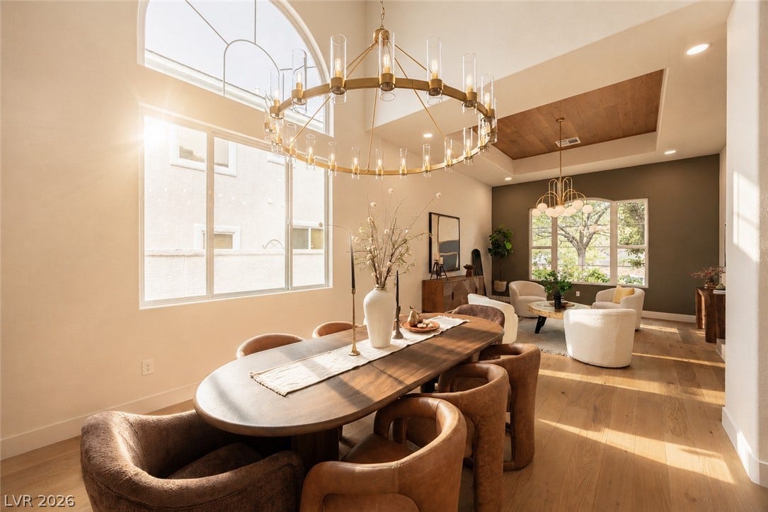 Natural light illuminates this dining area, featuring a grand chandelier and high ceilings with wood accents.