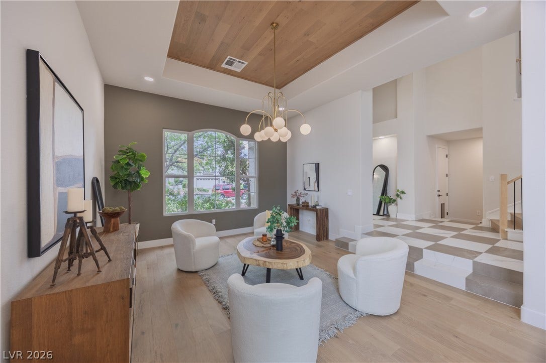 Living room featuring a wood tray ceiling, suspended lighting, and light wood-style floors
