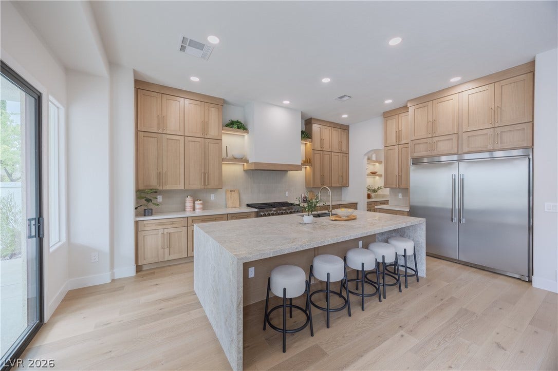 Kitchen with stainless steel appliances, light stone counters, light wood finished floors, an island with sink, and a kitchen breakfast bar