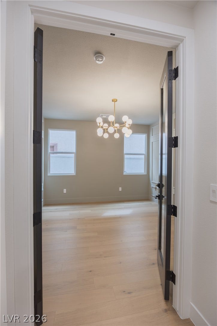 Hallway with light wood-style flooring, suspended lighting, and healthy amount of natural light