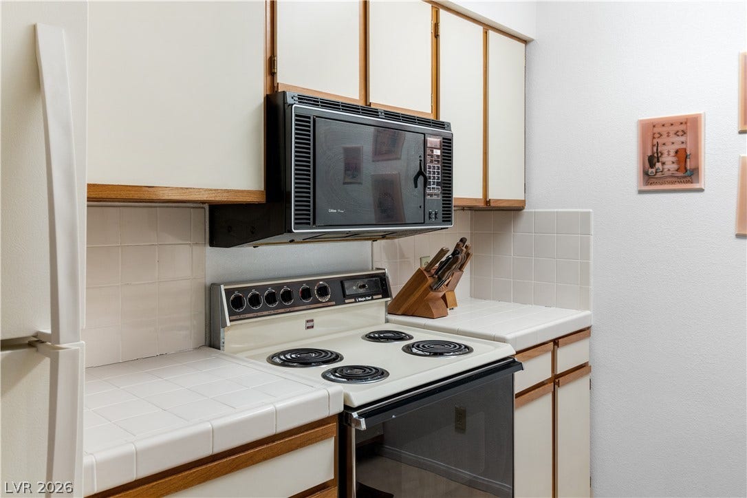 Kitchen featuring electric stove, black microwave, freestanding refrigerator, decorative backsplash, and tile counters