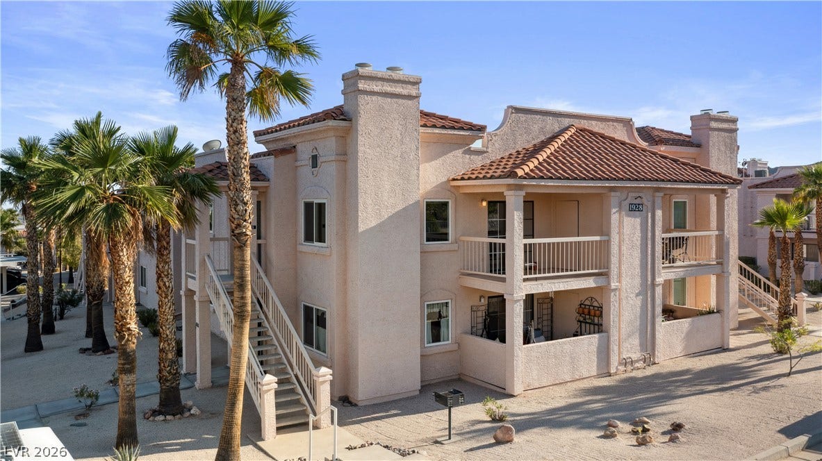 Back of house with stucco siding, a balcony, stairs, and a chimney