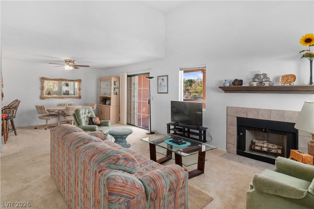 Carpeted living room featuring a fireplace and a ceiling fan