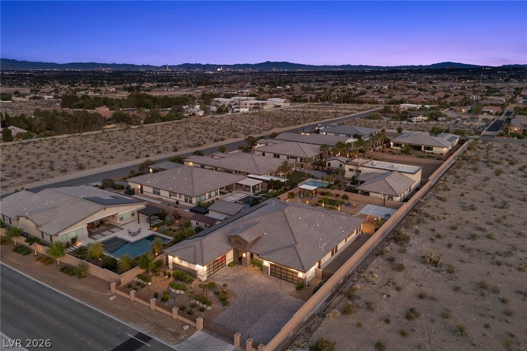 9841 W El Campo Grande Avenue, Las Vegas, NV 89149 An aerial perspective reveals a serene desert oasis with luxurious pools and a distant city glow.
