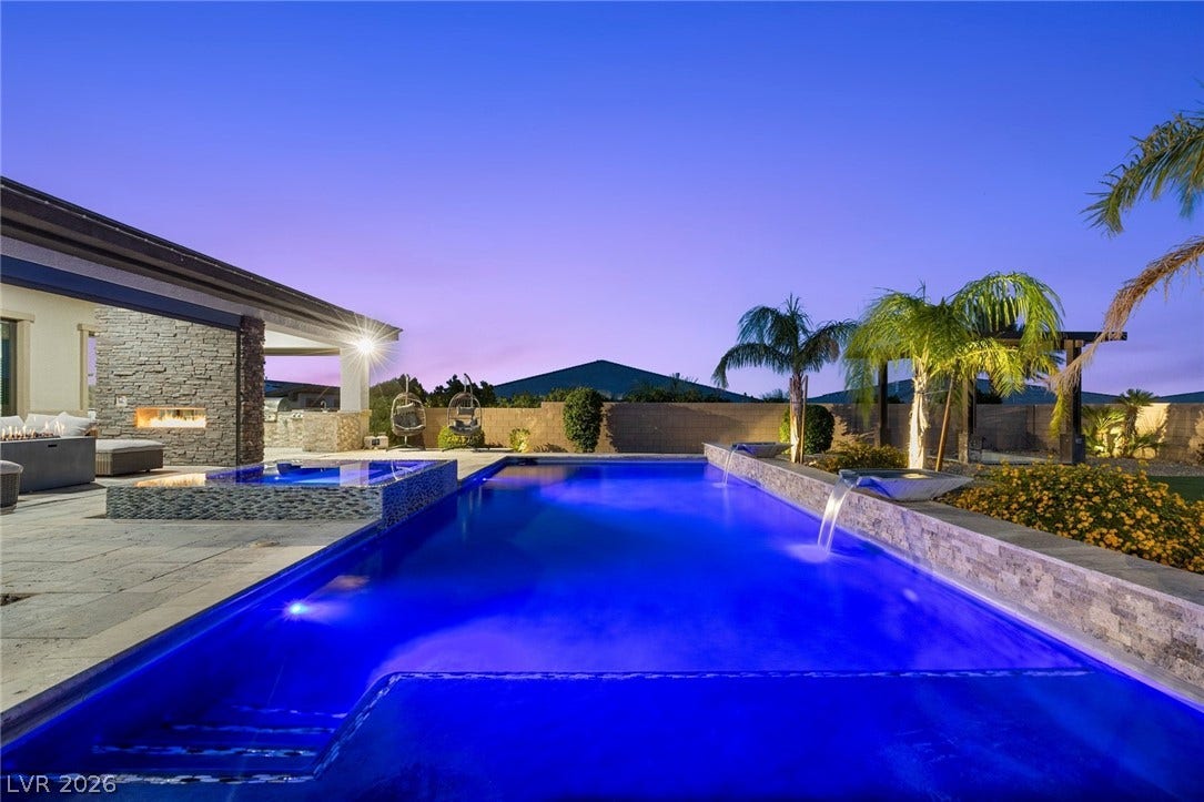 9841 W El Campo Grande Avenue, Las Vegas, NV 89149 An illuminated pool and spa invite relaxation under the evening sky, complemented by a covered patio with a fireplace.