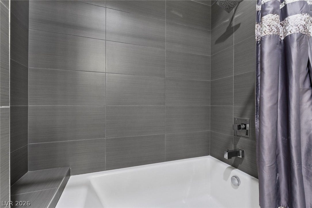 9841 W El Campo Grande Avenue, Las Vegas, NV 89149 A sleek, tiled tub and shower enclosure with integrated storage niche awaits relaxation.
