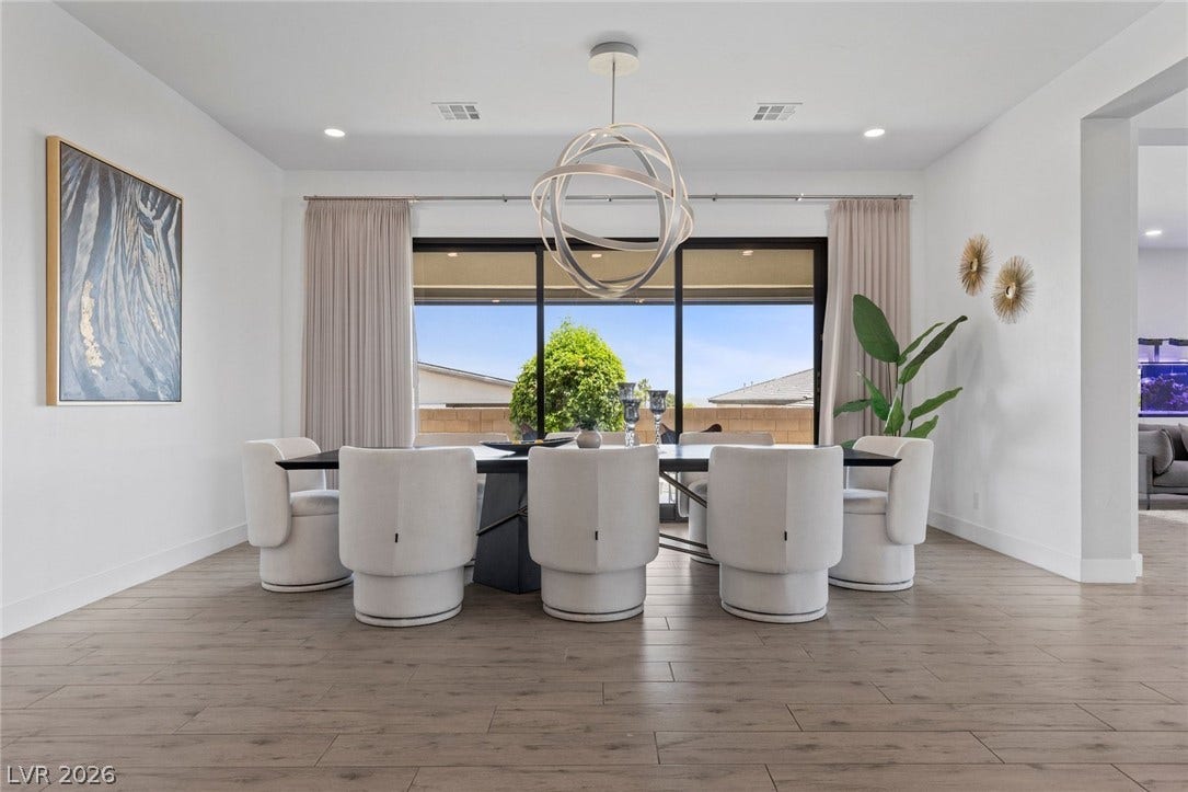 9841 W El Campo Grande Avenue, Las Vegas, NV 89149 A sophisticated dining area showcases a unique chandelier and broad windows offering natural light and backyard views.