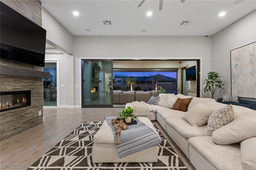 9841 W El Campo Grande Avenue, Las Vegas, NV 89149 A spacious living room features an inviting fireplace, high ceilings, and sliding glass doors revealing an outdoor oasis.