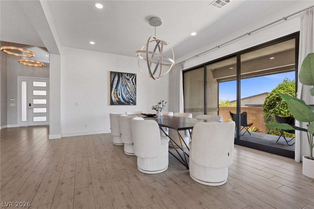 9841 W El Campo Grande Avenue, Las Vegas, NV 89149 A contemporary dining area features wood flooring, recessed lighting, and a modern chandelier, all complemented by large sliding glass doors.